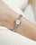 Handgelenk mit Damen-Armbanduhr: silbernes Edelstahlarmband, ovales Gehäuse, weißes Zifferblatt