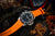 Herrenuhr mit orangefarbenem Kautschukband, schwarzem Zifferblatt und silberner Lünette
