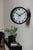 Horloge murale sur un mur avec un cadran blanc, des chiffres et des aiguilles noirs, un axe rouge