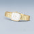 Montre pour femme avec bracelet métallique doré, boîtier rond-ovale et cadran blanc.