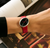 Armbanduhr am Handgelenk: rotes Lederband, schwarzes Zifferblatt mit roten Zeigern