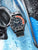 Montre avec cadran noir, lunette rouge, bracelet noir et couronne latérale