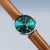 Herrenarmbanduhr schräg: grünes Zifferblatt, braunes Lederband, silberne Gehäusekanten.