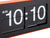 Gros plan d'une horloge murale : chiffres rabattables 10:10 sur un cadran noir, bord orange