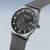 Herrenuhr Nahansicht: schwarzes Zifferblatt, orange Zeiger, rundes Gehäuse und Meshband