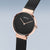Montre femme en gros plan : cadran noir, aiguilles or rose, bracelet milanais noir
