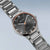 Herrenuhr seitlich im Detail: Metallarmband, schwarzes Zifferblatt mit orangefarbenen Markierungen