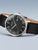 Herrenuhr mit schwarzem Zifferblatt und schwarzem Lederarmband, braune Unterseite sichtbar