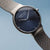 Herrenuhr im Schrägansicht: blaues Zifferblatt, silbernes Milanaiseband, runde Lünette.