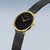 Montre Bering pour femme, vue de biais : cadran noir, lunette dorée, bracelet milanais noir.