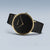 Montre pour femme avec cadran noir, lunette dorée et bracelet milanais noir.