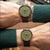 Montre pour homme au poignet avec cadran vert, aiguilles orange et bracelet en cuir marron