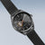 Montre automatique homme avec cadran sombre, balancier apparent et bracelet milanais noir