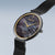 Montre pour femme avec cadran sombre, aiguilles dorées et couronne latérale, bracelet milanais