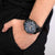 Montre chronographe au poignet : cadran bleu, boîtier noir, bracelet en cuir