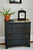 Montre de table sur une commode bleu foncé à côté d'une plante en pot, boîtier noir, cadran floral