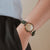 Damen-Armbanduhr am Handgelenk mit grünem Lederarmband und rundem Holz-Zifferblatt