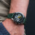 Holzkern Herrenarmbanduhr am Handgelenk mit grünem Lederband, schwarzem Zifferblatt und gelben Zeigern