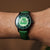 Unisex-Armbanduhr am Handgelenk: grünes Lederarmband, Zifferblatt mit Avatar-Emblem