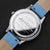 Rückseite einer Armbanduhr: silbernes Gehäuse mit Gravur, blaues Lederarmband mit Dornschließe