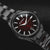 Herrenuhr mit schwarzem Armband, rundem Gehäuse und schwarzem Zifferblatt mit rotem Muster