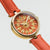 Damenarmbanduhr Close-up: goldfarbener Rand, rotes Lederband, blütenartiges Zifferblatt