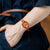 Damenarmbanduhr am Handgelenk: rotes Lederband, goldfarbener Rahmen und orange-rotes Zifferblatt