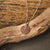 Collier avec pendentif rond en bois sur chaîne en argent, posé sur une branche en bois