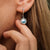 Boucle d'oreille argentée avec pendentif rond et pierre bleue, sur créole