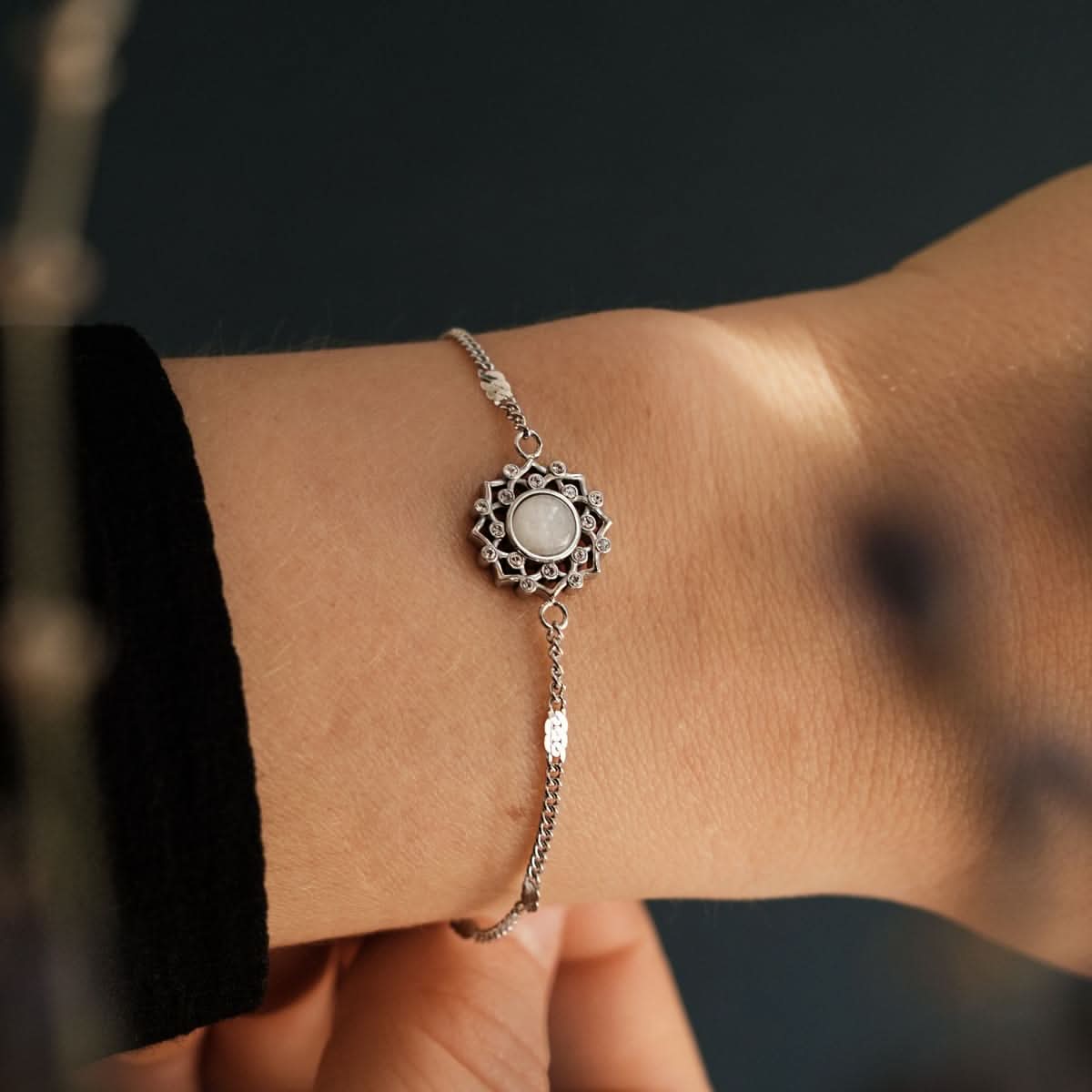 Bracelet en argent avec cabochon rond gris dans un ornement floral et une chaîne fine.