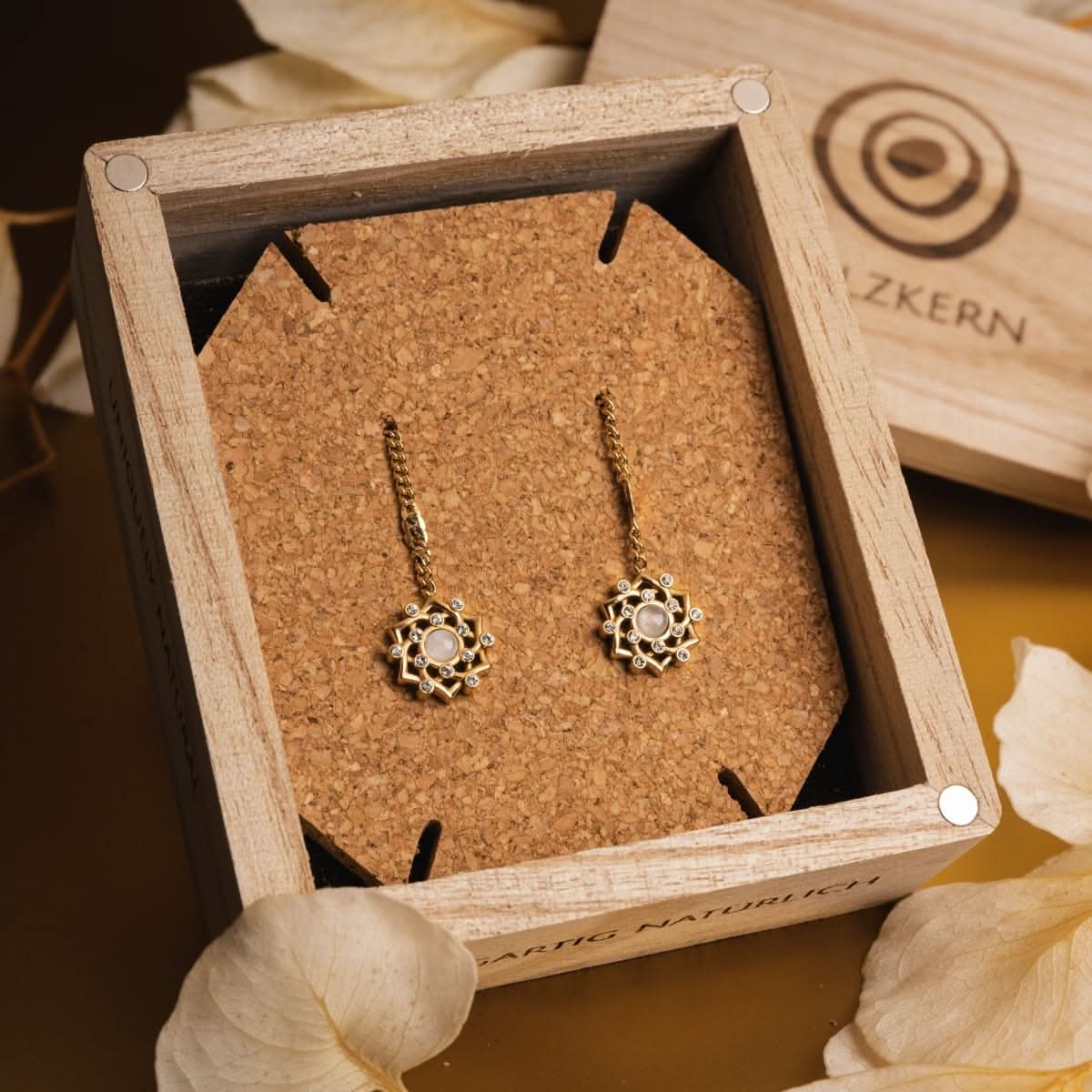 Boucles d'oreilles dorées avec monture circulaire couleur pierre de lune et chaîne, dans une boîte à bijoux