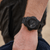 Montre pour homme au poignet : montre de sport noire avec cadran sombre et bracelet noir.