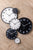 Horloge murale avec cadran blanc et cadre noir, à côté d'autres horloges en noir/blanc