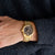 Herrenuhr am Handgelenk: goldfarbenes Metallarmband und schwarzes Zifferblatt mit Indexen