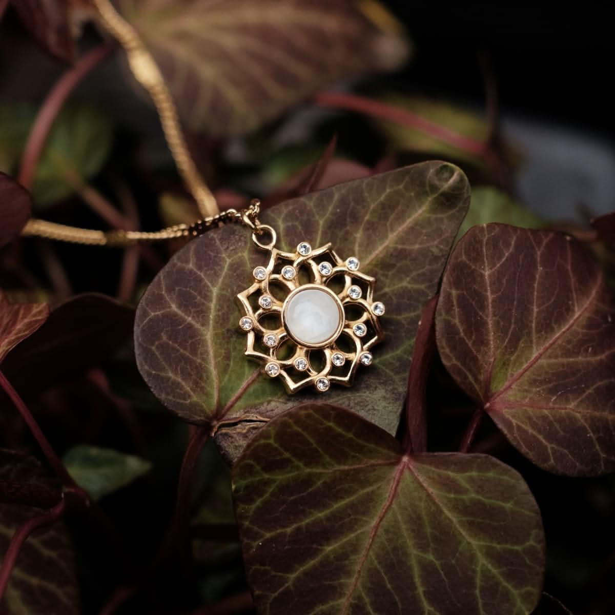 Collier doré avec cabochon rond blanc dans un pendentif floral orné de pierres scintillantes