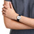 Mondaine Damenuhr am Handgelenk: schwarzes Armband, weißes Zifferblatt mit roten Zeigern und Akzenten.