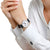 Mondaine Classic Damenuhr am Handgelenk mit schwarzem Lederband und weißem Zifferblatt.