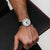 Herrenuhr am Handgelenk: schwarzes Armband mit rotem Rand, weißes Zifferblatt, Datum „SAT 3“