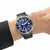 Montre homme au poignet avec bracelet en caoutchouc noir, cadran bleu et aiguilles lumineuses.