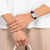 Poignet avec montre, bracelet en cuir noir et boîtier argenté sur chemise blanche