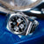 Montre homme avec bracelet en métal argenté, cadran noir et aiguille des secondes orange