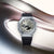 Herrenuhr in Frontansicht mit grauem Zifferblatt, schwarzem Band und Digitalanzeigen.