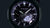 Herrenuhr mit dunklem Zifferblatt und violetten Akzenten, schwarzem Gehäuse und Band.