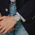 Am Handgelenk getragene Casio G-Shock Herrenuhr mit blauem Zifferblatt und Metallarmband.