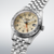 Herren-Armbanduhr im Nahblick: silbernes Gehäuse, beiges Zifferblatt, orange GMT-Hand