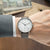 Montre pour homme au poignet : bracelet en cuir marron, boîtier argenté, cadran blanc avec index.
