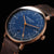 Montre homme en gros plan : cadran bleu, boîtier doré-brun et bracelet en cuir marron.