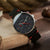 Montre homme de profil au poignet : cadran noir, bracelet en cuir noir avec accents rouges