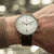 Montre pour homme au poignet : bracelet en cuir marron, cadran blanc, aiguilles de chronographe rouges