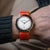 Montre homme au poignet avec bracelet textile orange, cadran rond blanc